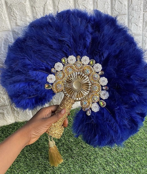 A rich navy feather hand fan with an ornate jeweled gold centerpiece and handle